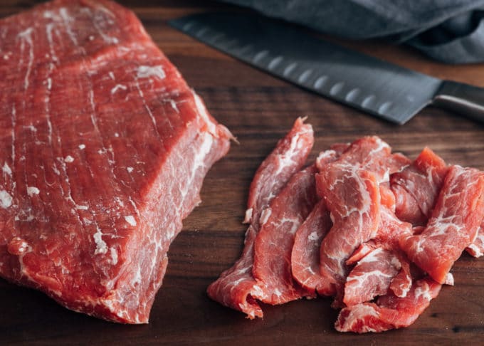 sliced flank steak on a cutting board with a santoku knife