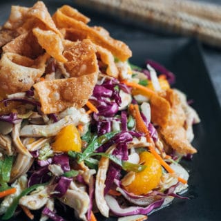 chinese chicken salad with crispy wonton strips on a black plate