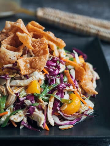 chinese chicken salad with crispy wonton strips on a black plate
