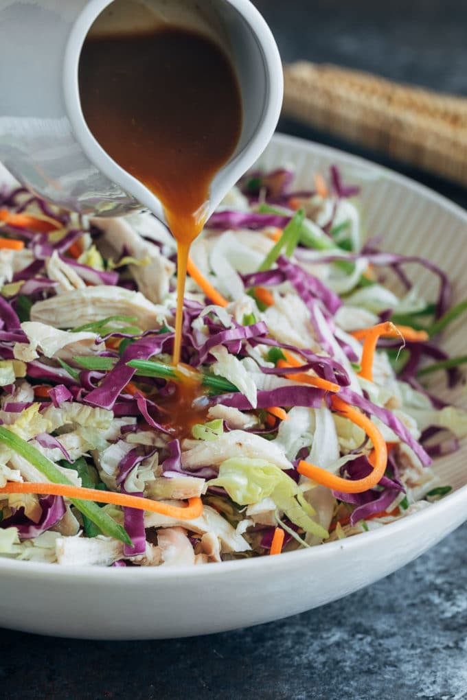 pouring plum vinaigrette over tossed chicken salad in a large bowl