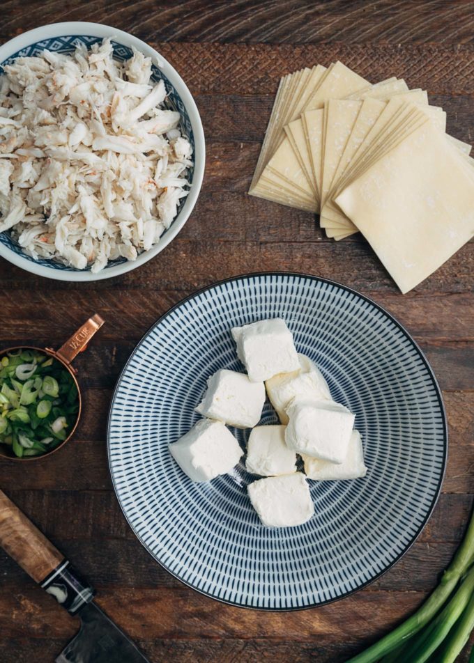 ingredients for crab rangoon in bowls on a wood board