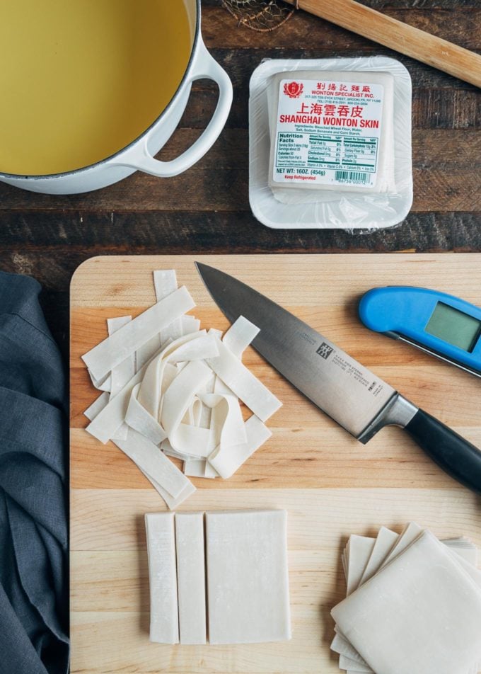 cut and whole wonton wrappers on a cutting board with a knife