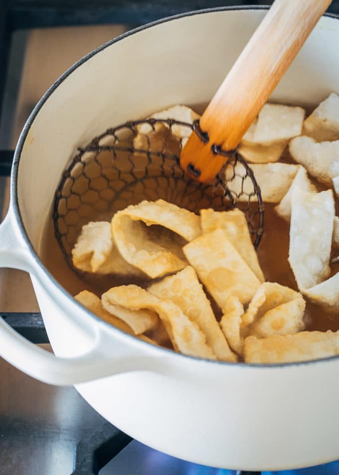 wonton strips being fried in a white pot with a spider spatula
