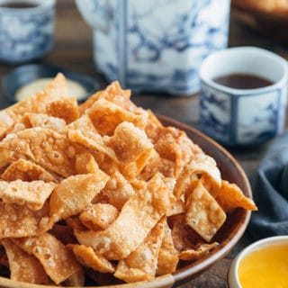 crispy fried wonton strips in a bowl with duck sauce and cups of tea