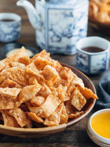 crispy fried wonton strips in a bowl with duck sauce and cups of tea