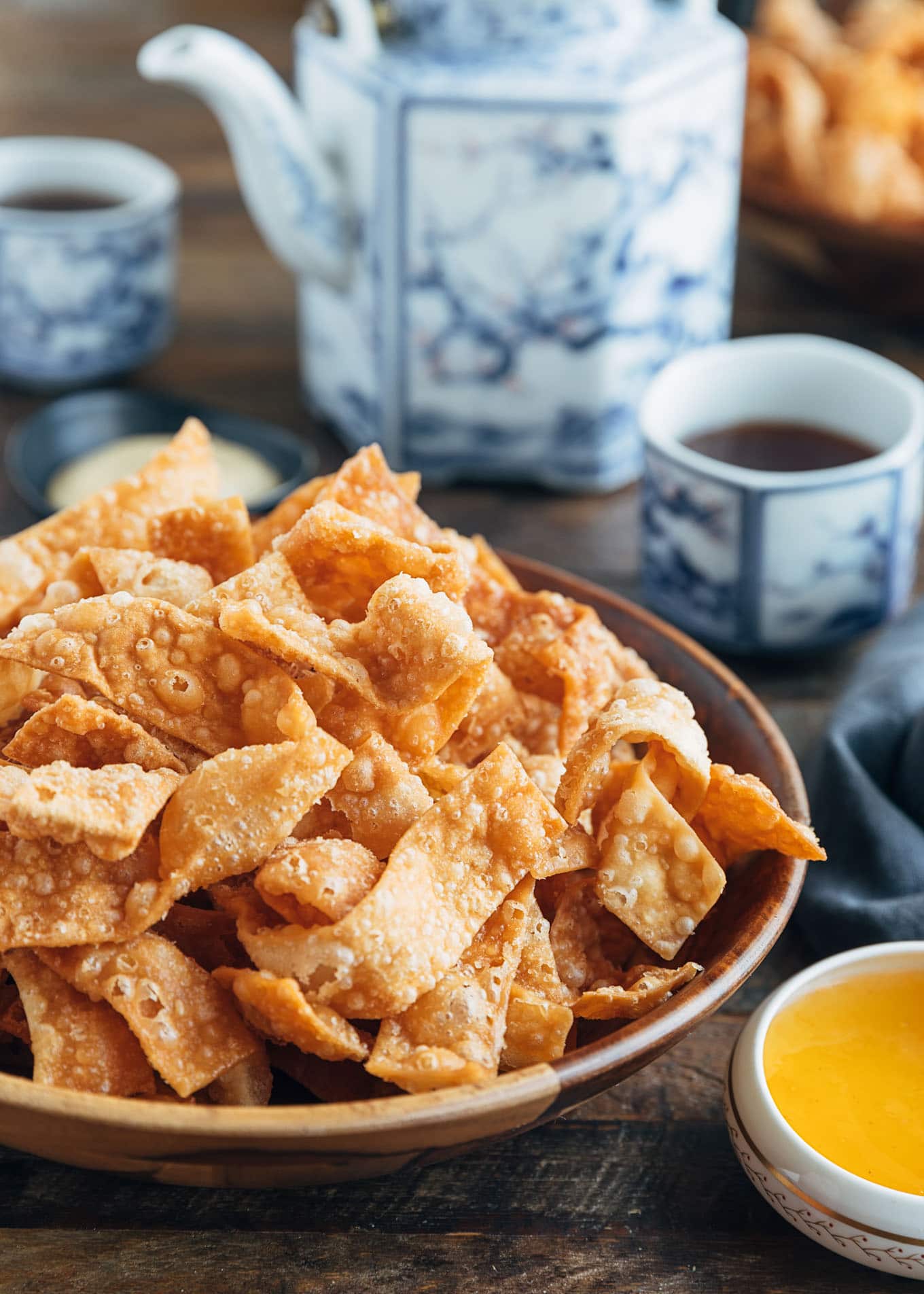 crispy fried wonton strips in a bowl with duck sauce and cups of tea