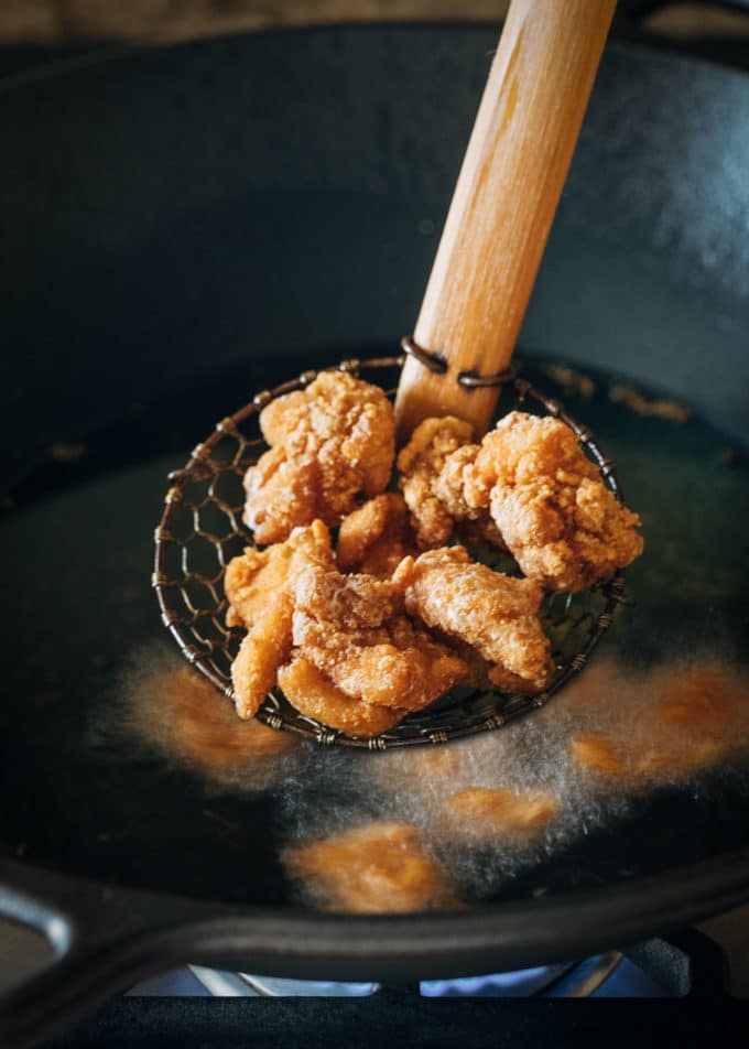 fried chicken thigh pieces in a spider strainer