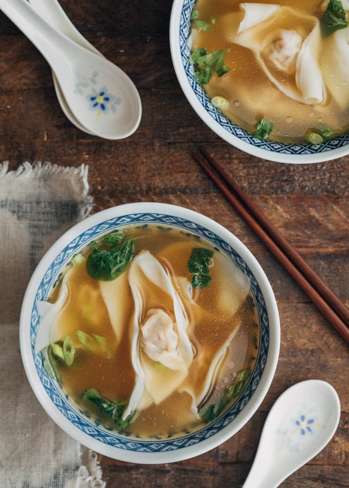 Schüssel mit hausgemachter Wonton-Suppe mit Babyspinat und geschnittenen Frühlingszwiebeln