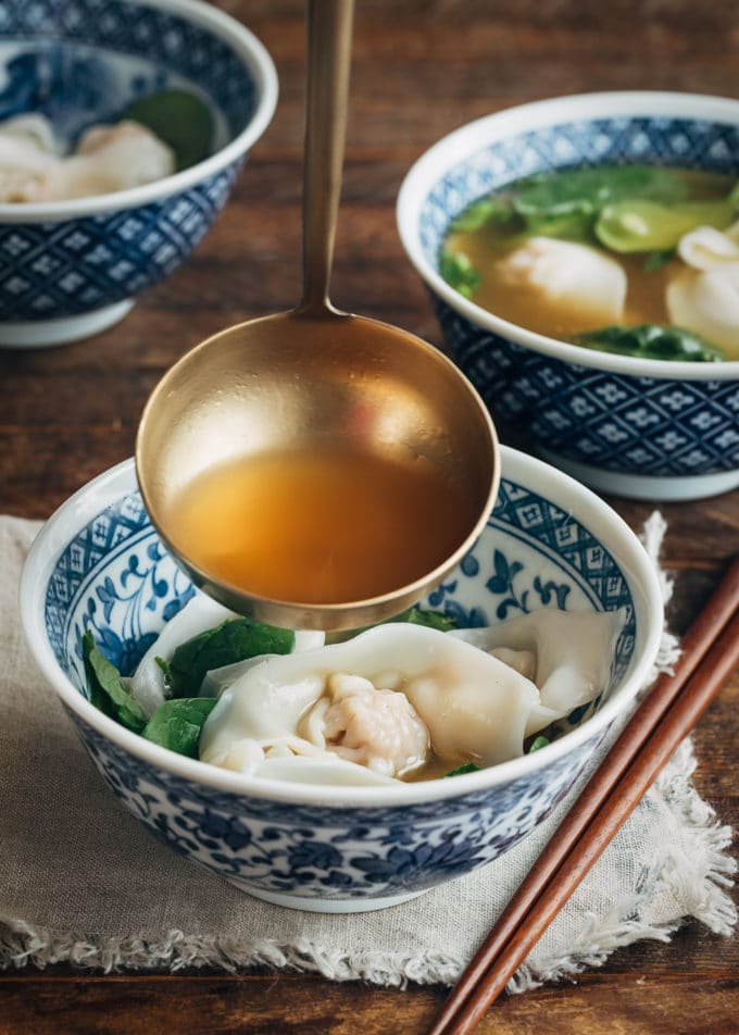 ladling broth over wontons and baby spinach in a serving bowl