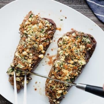 slicing blue cheese crusted steak on a white serving platter