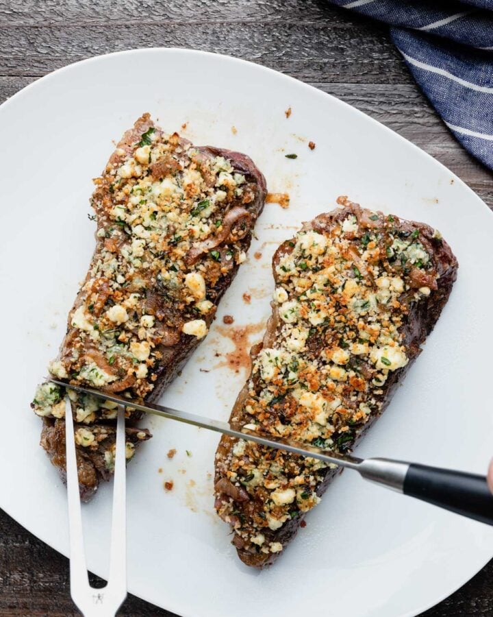 slicing blue cheese crusted steak on a white serving platter