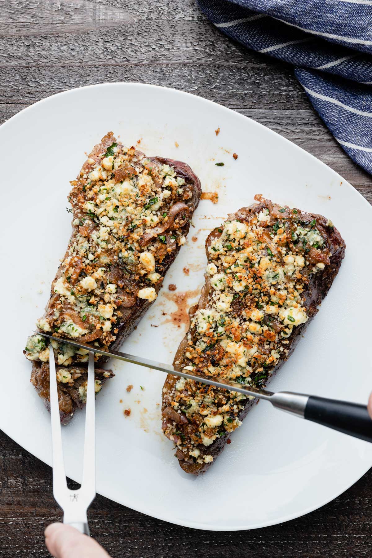 slicing blue cheese crusted steak on a white serving platter