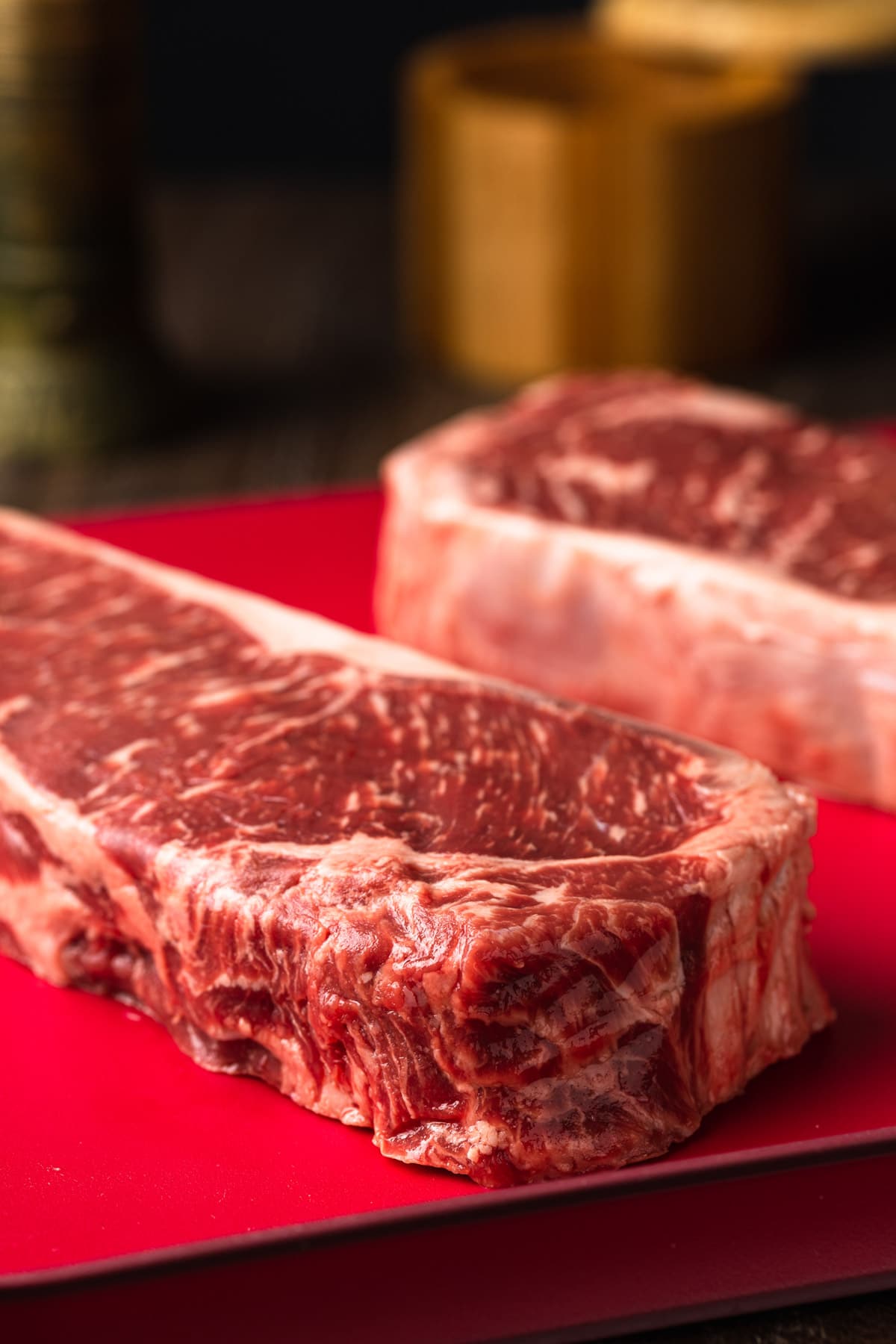 uncooked new york strips steaks on a red cutting board