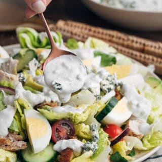 homemade blue cheese dressing being drizzled over a house salad