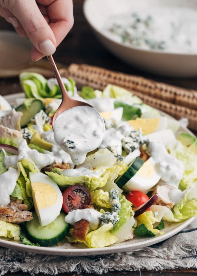 homemade blue cheese dressing being drizzled over a house salad