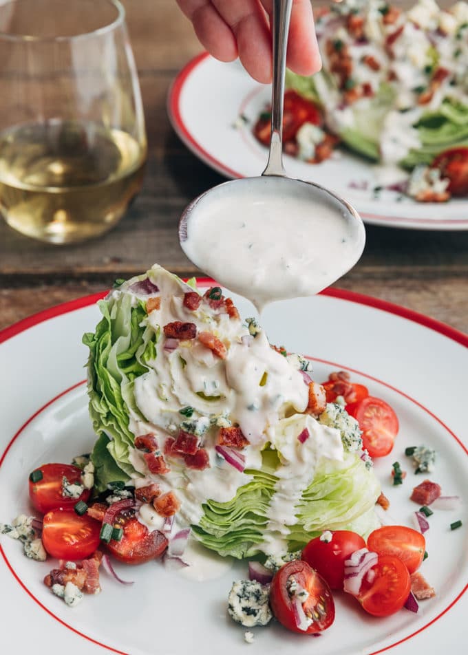 ladleful of blue cheese dressing pouring onto a loaded wedge salad