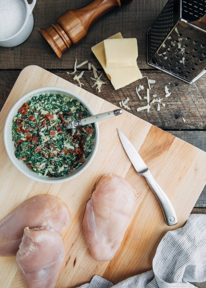 raw chicken breasts on a board with a bowl of creamed spinach filling