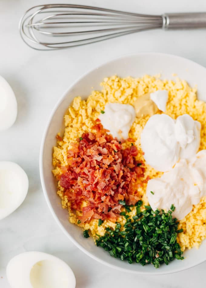crumbled egg yolks in a bowl with bacon, mayonnaise, sour cream, and chives