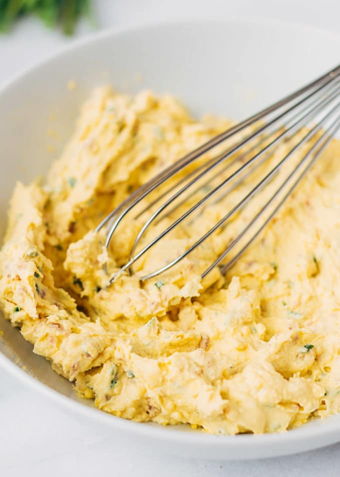 bacon deviled egg filling in a bowl with a whisk