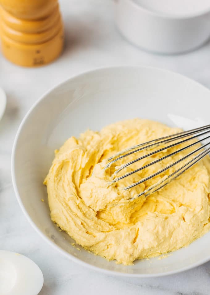 deviled egg filling in a white bowl with a whisk