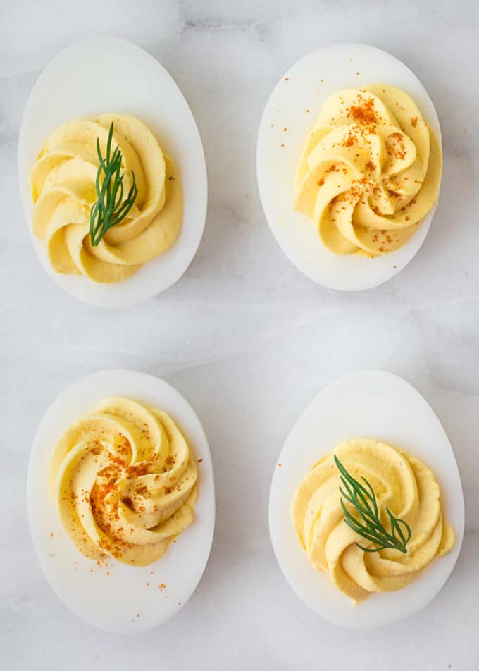 four deviled eggs with dill sprigs and paprika
