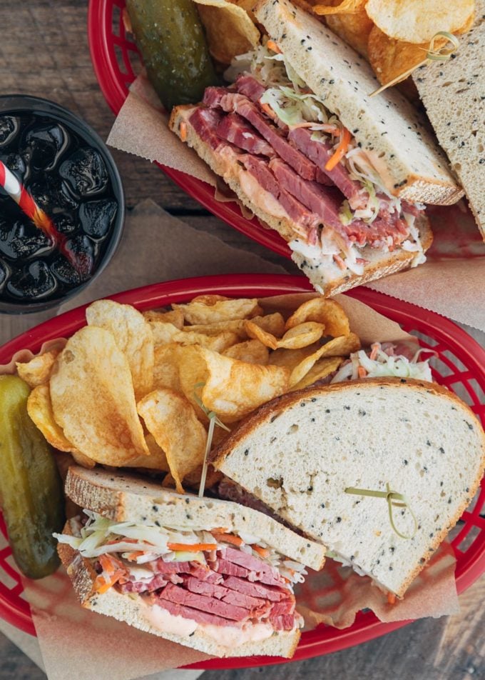 corned beef sandwiches in serving baskets with chips and pickles