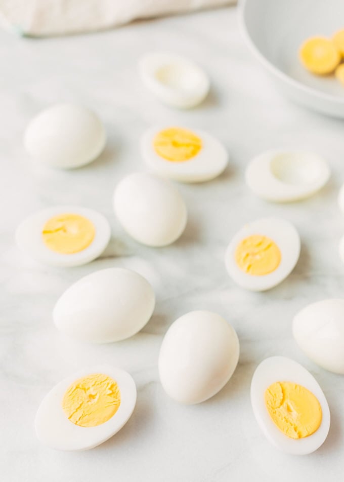 whole and halved hard boiled eggs on a white marble board