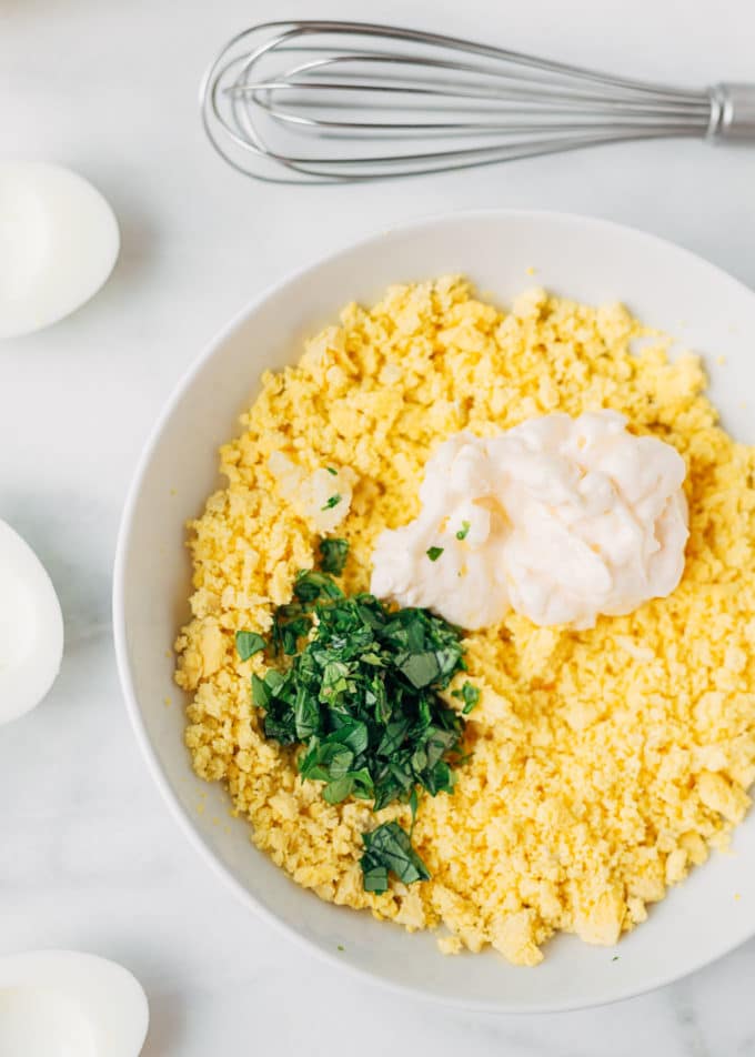 crumbled egg yolks in a bowl with chopped basil, mayonnaise, and garlic