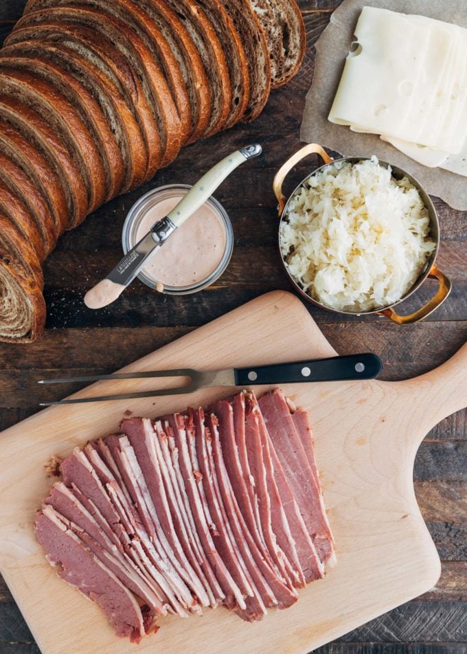 sliced corned beef on a board with bowls of sauerkraut and russian dressing