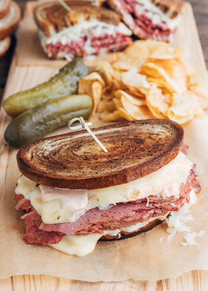 reuben sandwich on a board with chips and pickles