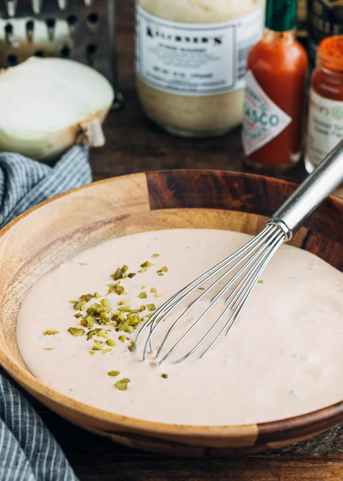 mixed homemade Russian dressing in a wooden bowl with a whisk. A few chopped cornichons are on the top of the dressing.