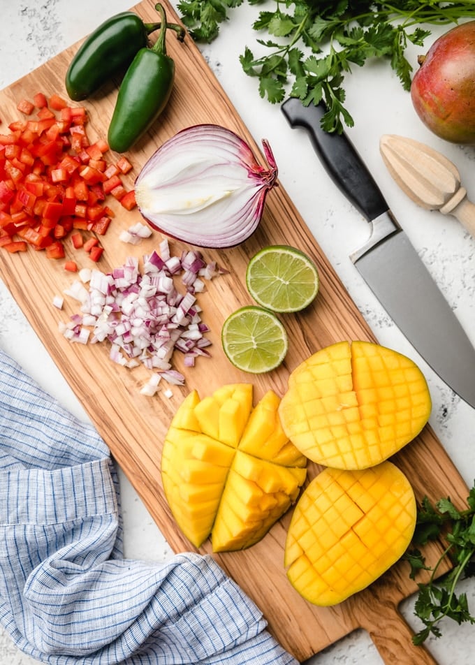 chopped bell pepper, red onion, and scored mangoes on a wood cutting board