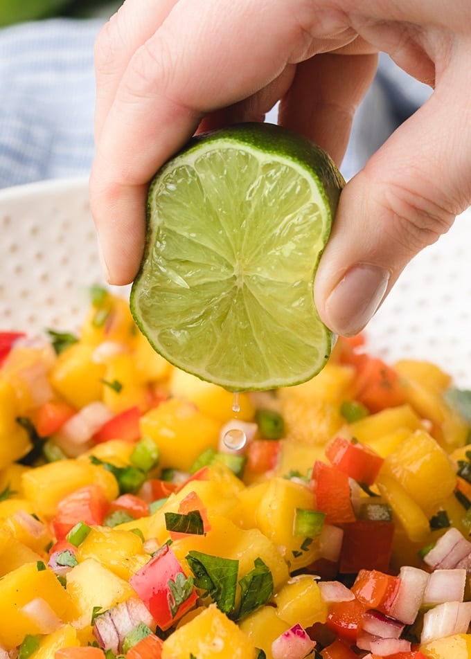 lime juice being squeezed into a bowl of mango salsa
