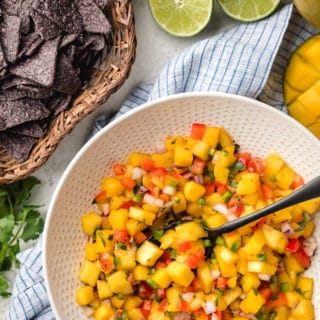 mango salsa in a bowl next to a basket of blue corn chips