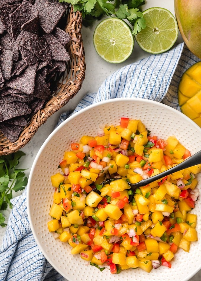 mango salsa in a bowl next to a basket of blue corn chips