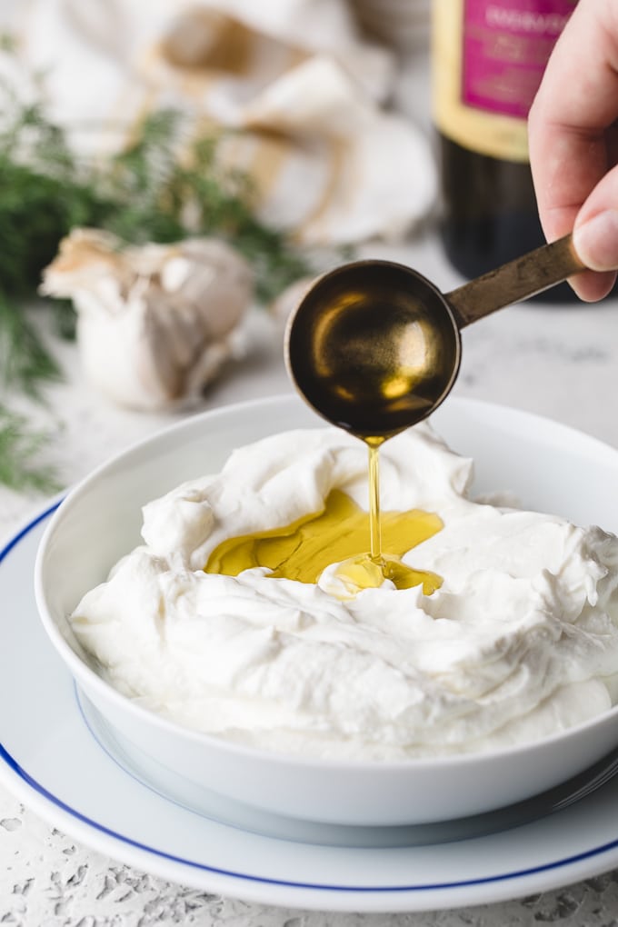 olive oil being drizzled into a bowl of Greek yogurt
