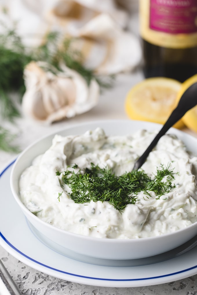 chopped dill added to a bowl of tzatziki sauce with a spoon