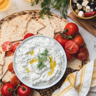 overhead of homemade tzatziki sauce in a bowl with tomatoes and torn pita bread on the side