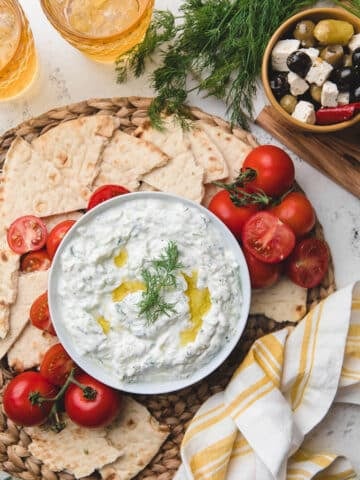 overhead of homemade tzatziki sauce in a bowl with tomatoes and torn pita bread on the side