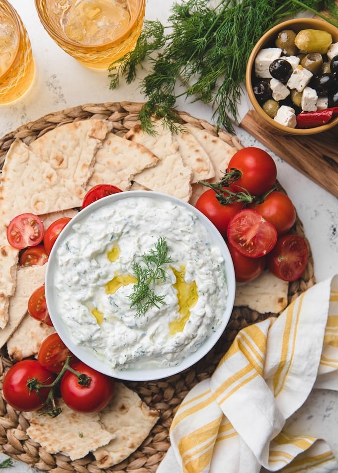 overhead of homemade tzatziki sauce in a bowl with tomatoes and torn pita bread on the side