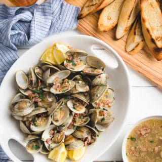 beer steamed littleneck clams in a white serving dish with a board of grilled bread slices