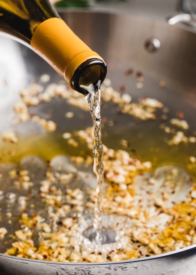 pour shot of white wine into a pan of sauteed garlic