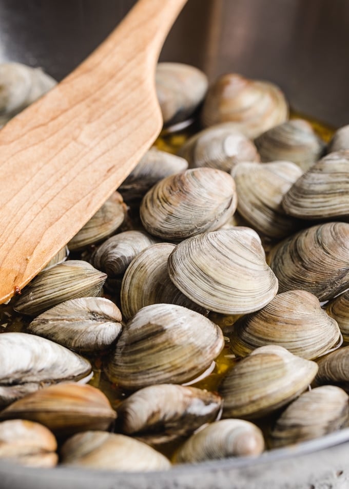 littleneck clams in a stainless steel pan with a wooden spoon