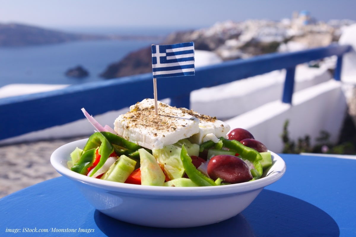 greek salad with a greek flag pick on a blue table overlooking an ocean sean