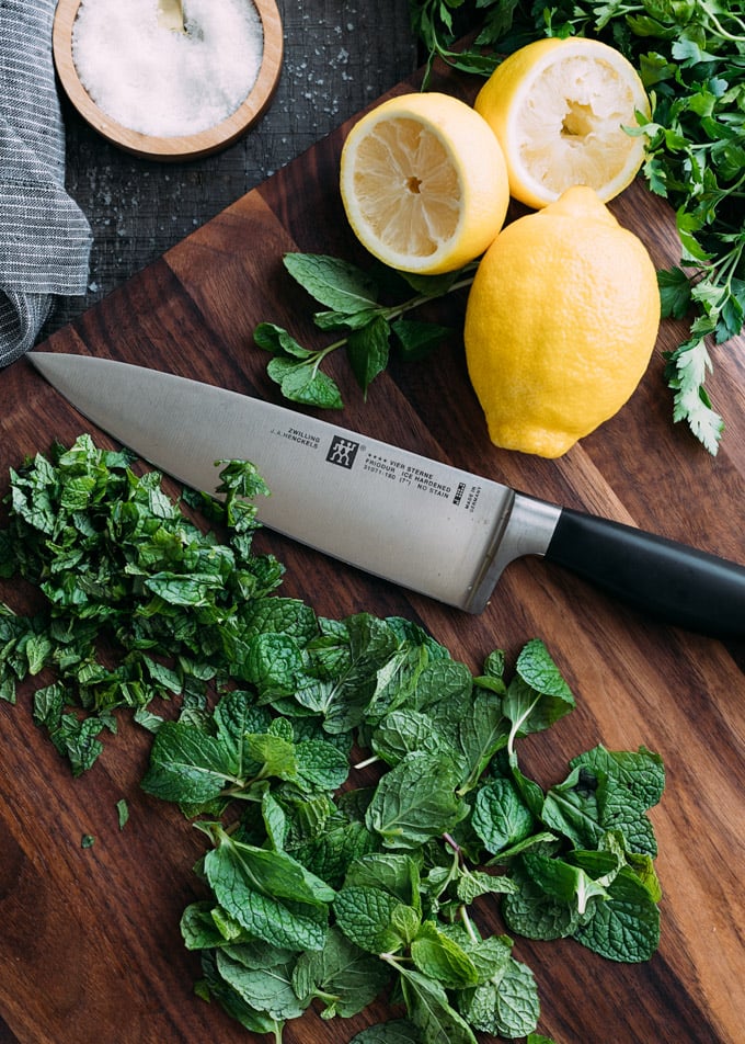 chopped mint on a wood cutting board with a chef's knife and lemons
