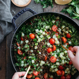 overhead photo of tossing lentil tabbouleh salad in a cast iron pan with gold colored spoons