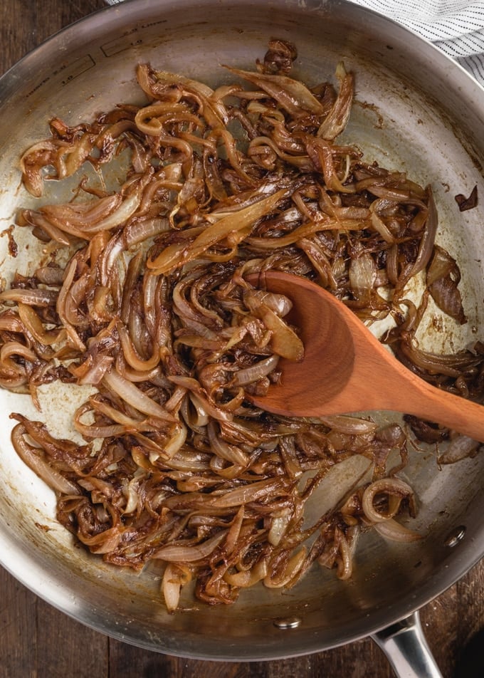 overhead closeup of caramelized onions in a pan with a wooden spoon