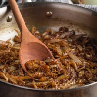 caramelized onions in a stainless steel skillet with a wooden spoon