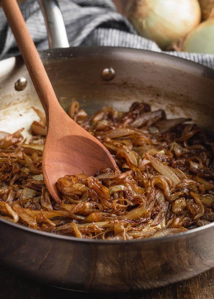 caramelized onions in a stainless steel skillet with a wooden spoon