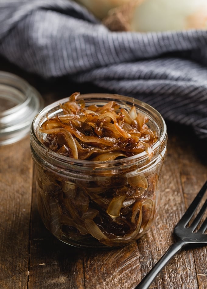 glass jar of caramelized onions on a wood board next to a black fork